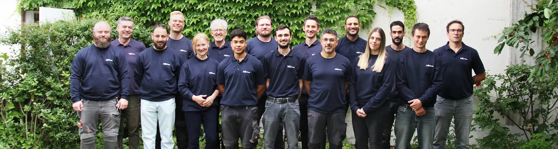 Das gesamte Team der Kreuz GmbH aus Schallstadt steht in dunklen Hemden vor einen grün bewachsenen Mauer.