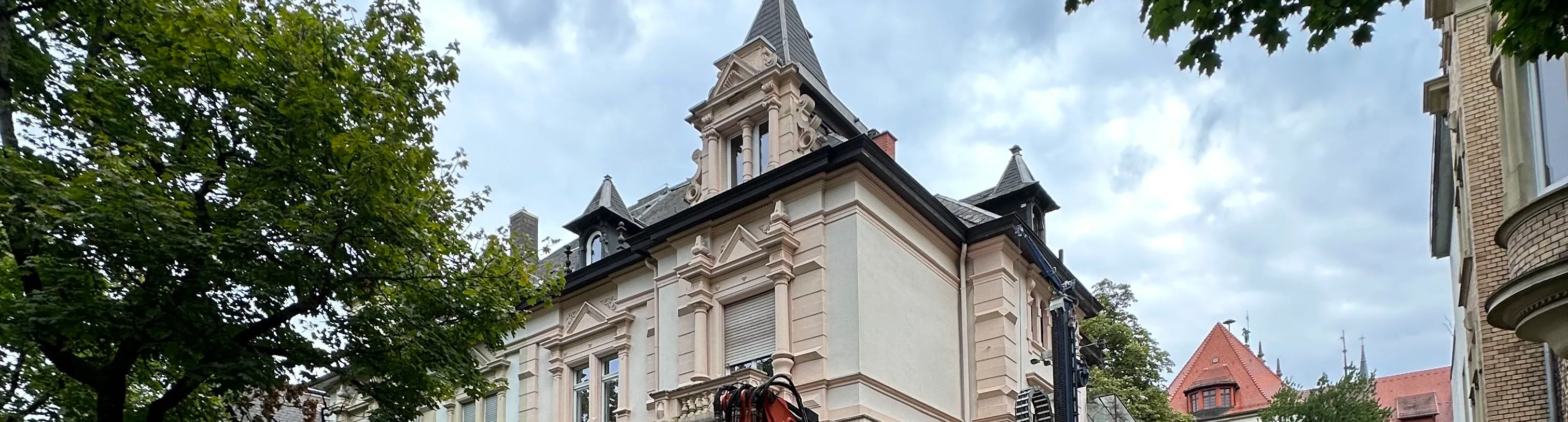 Ansicht eines historischen Wohn- und Geschäftsgebäudes mit reich verzierten Fassadenelementen, Erkern und Turmaufbau, aufgenommen von der Straßenseite.