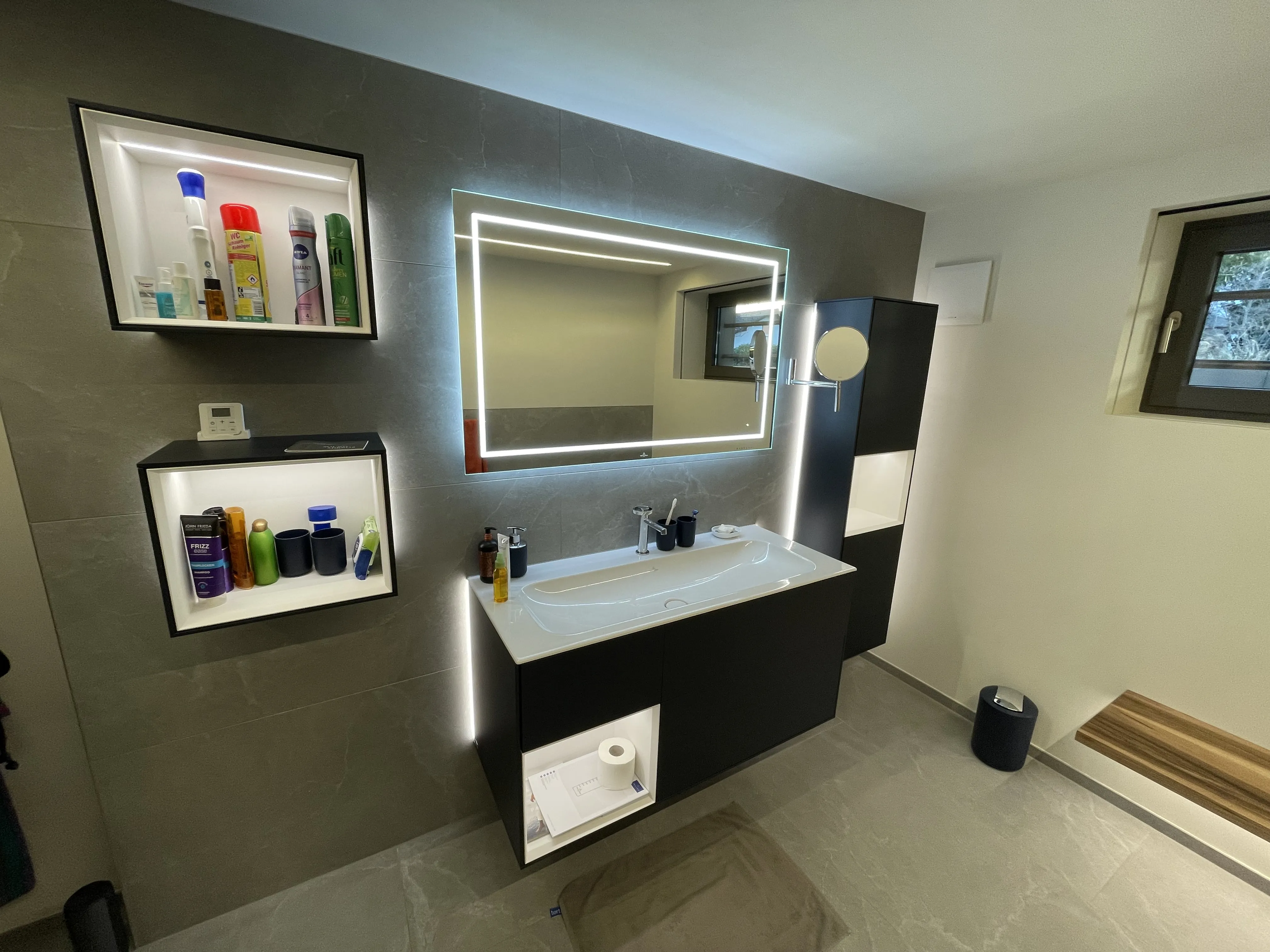 Moderner Waschtisch mit LED-Spiegel und beleuchteten Wandnischen im Badezimmer.