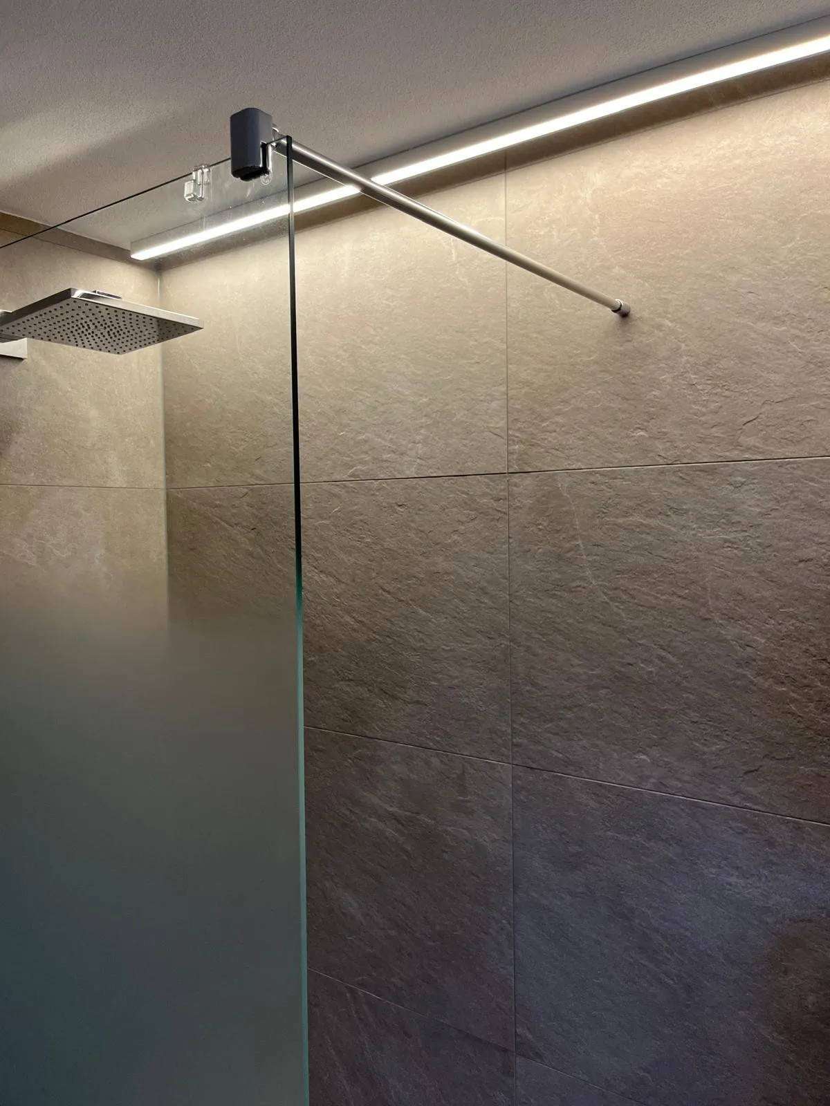 Walk-In Dusche mit Glaswand und indirekter LED-Lichtleiste an der Decke.