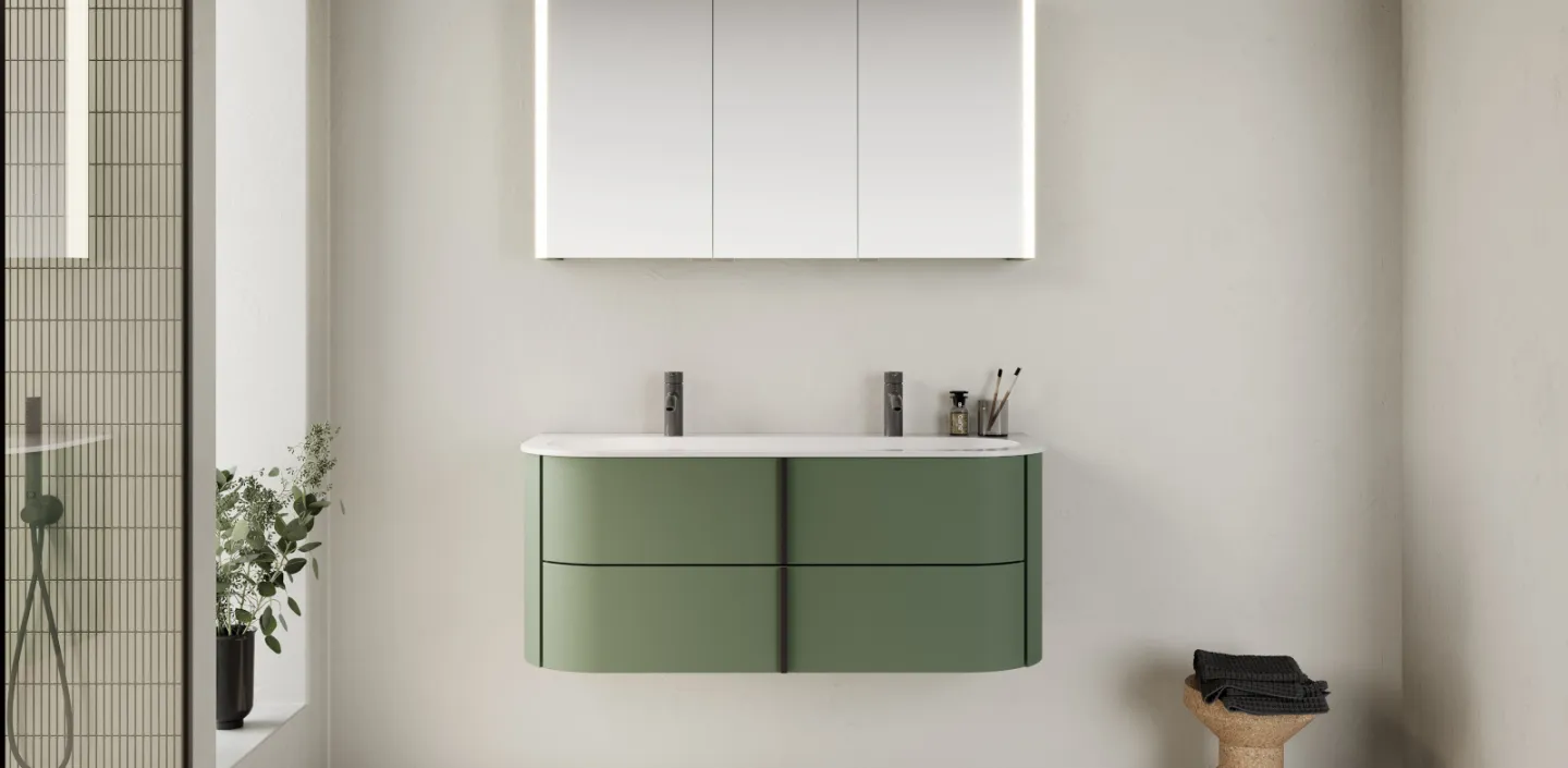 Ein modernes Badezimmer mit einem schwebenden, grünen Waschtisch, der mit einer weißen Oberfläche und zwei schlichten, schwarzen Armaturen ausgestattet ist.