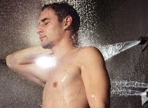 Ein Mann mit geschlossenen Augen steht unter einer Dusche mit Seitenbrausen, die seinen Körper von allen Seiten mit Wasserstrahlen erfrischen.