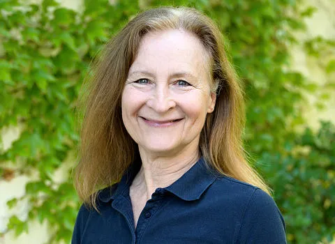 Portrait der Badexpertin Ruth Kreuz vor einer mit grünen Blättern bedeckten Mauer.