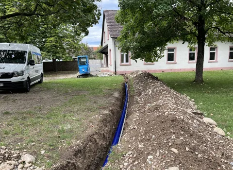 Ein langer, frisch ausgehobener Graben zieht sich durch den Garten eines Wohnhauses, in dem ein blaues Kabel verlegt wurde.