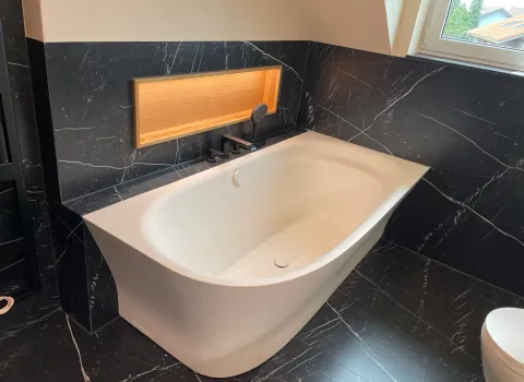 Eine moderne weiße Badewanne in einem Badezimmer mit großen Fliesen in dunkler marmoroptik.