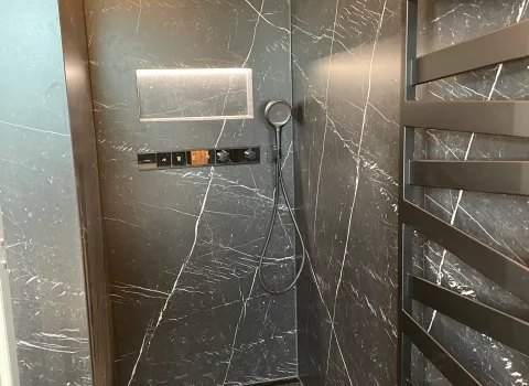 Eine bodengleiche Dusche in dunkler Marmoroptik mit Design-Heizkörper und beleuchteter Ablage.