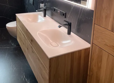 Ein moderner Waschtisch-Unterbauschrank in Holzoptik mit dunklen Armaturen und Fliesen im Marmoroptik.