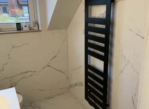 Schwarzer Handtuchheizkörper in modernem Badezimmer mit Marmoroptik-Fliesen.