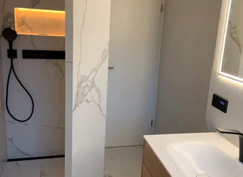 Walk-in Dusche mit schwarzer Regendusche und beleuchteter Nische im modernen Bad.