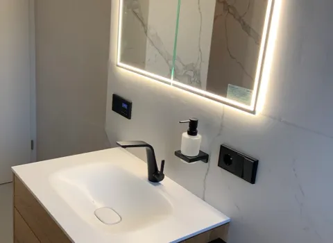 Moderner Waschtisch mit Holzoptik und LED-Spiegel in minimalistischem Badezimmer.
