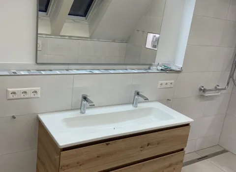 Doppelwaschbecken mit Holzunterschrank und großem LED-Spiegel im modernen Bad.