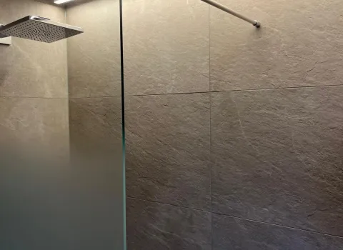 Walk-In Dusche mit Glaswand und indirekter LED-Lichtleiste an der Decke.