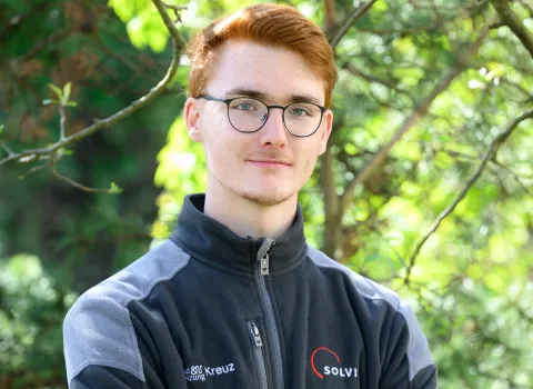 Teamportait eines jungen Kundendienst-Mitarbeiters der Kreuz GmbH vor grünen Blättern.
