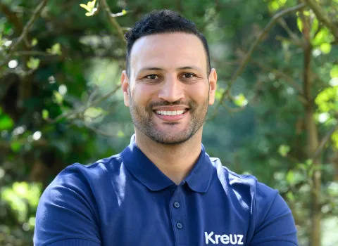 Teamportait eines Mitarbeiters der Kreuz GmbH vor grünen Blättern.
