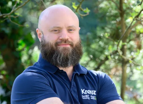 Teamportait eines Mitarbeiters der Kreuz GmbH vor grünen Blättern.