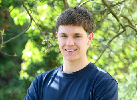 Teamportait eines jungen Mitarbeiters der Kreuz GmbH vor grünen Blättern.