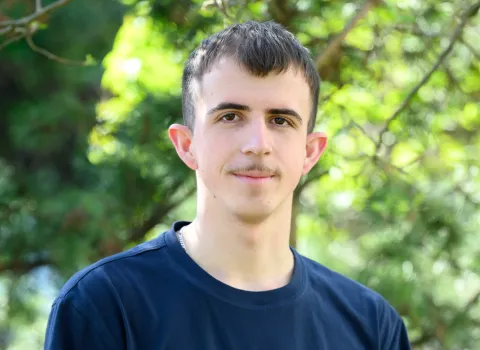Teamportait eines jungen Mitarbeiters der Kreuz GmbH vor grünen Blättern.