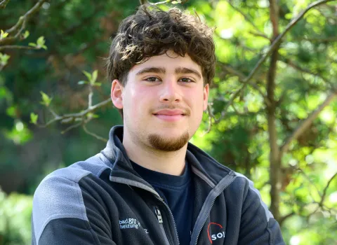 Teamportait eines jungen Kundendienst-Mitarbeiters der Kreuz GmbH vor grünen Blättern.