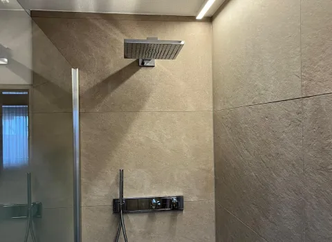 Moderne Regendusche mit Edelstahlarmatur und indirekter LED-Beleuchtung an großformatigen Fliesen.