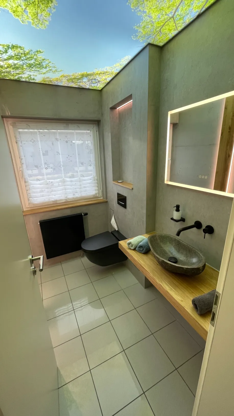 Ein Gästebad mit Leuchtspiegel und Naturstein-Waschbecken.