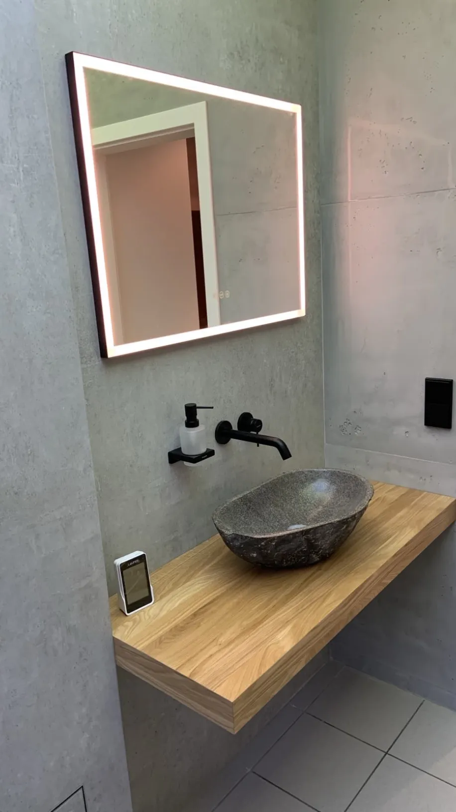 Ein Gästebad mit Leuchtspiegel und Naturstein-Waschbecken.