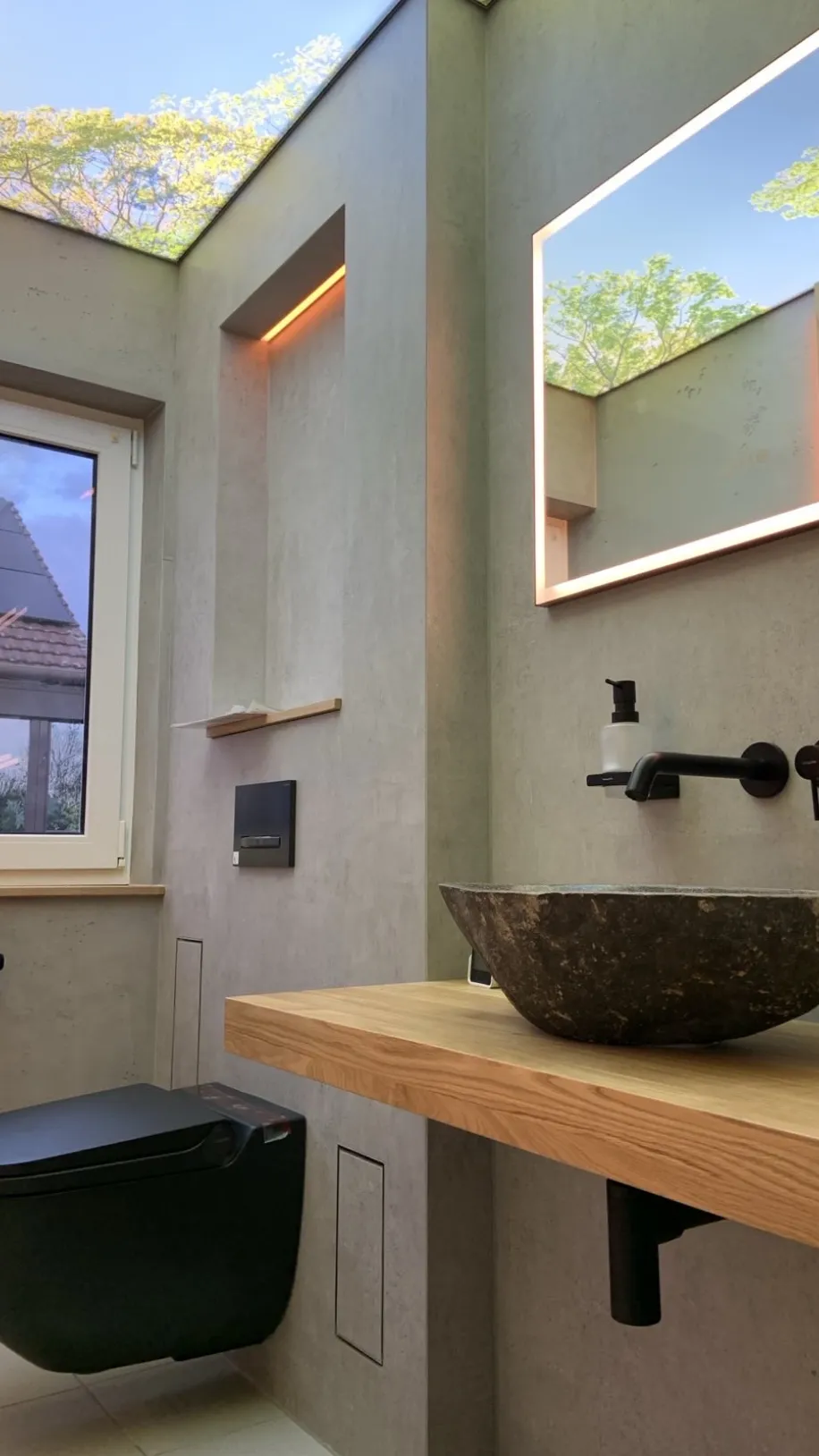 Ein Gästebad mit Leuchtspiegel und Naturstein-Waschbecken.