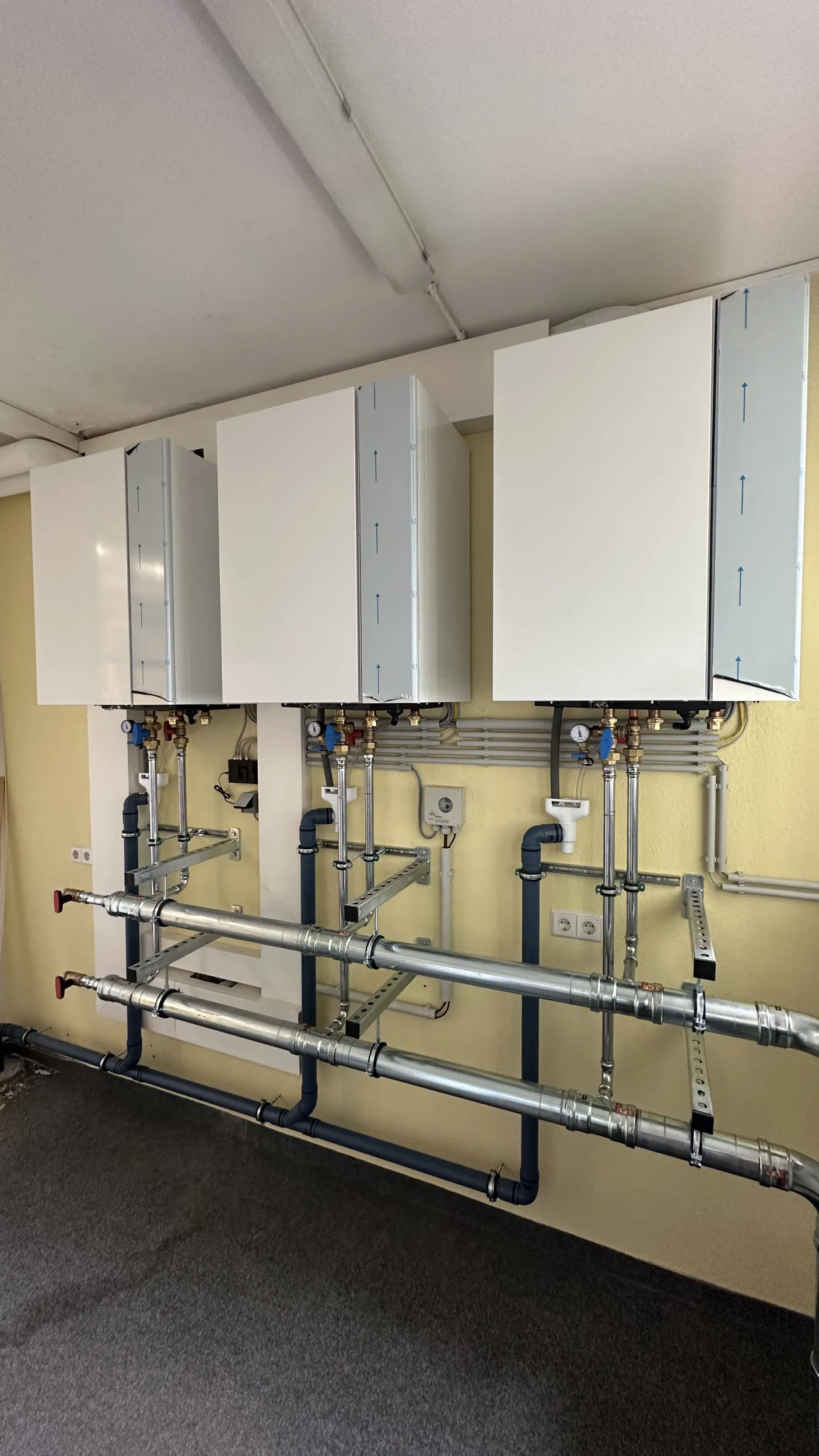 Drei wandhängende weiße Heizgeräte sind nebeneinander an einer gelb gestrichenen Wand montiert.