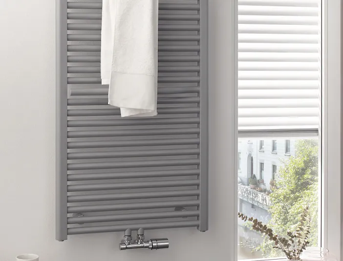 In einem hellen Badezimmer hängt ein grauer HSK Line Plus Heizkörper mit einem weißen Handtuch daran. 