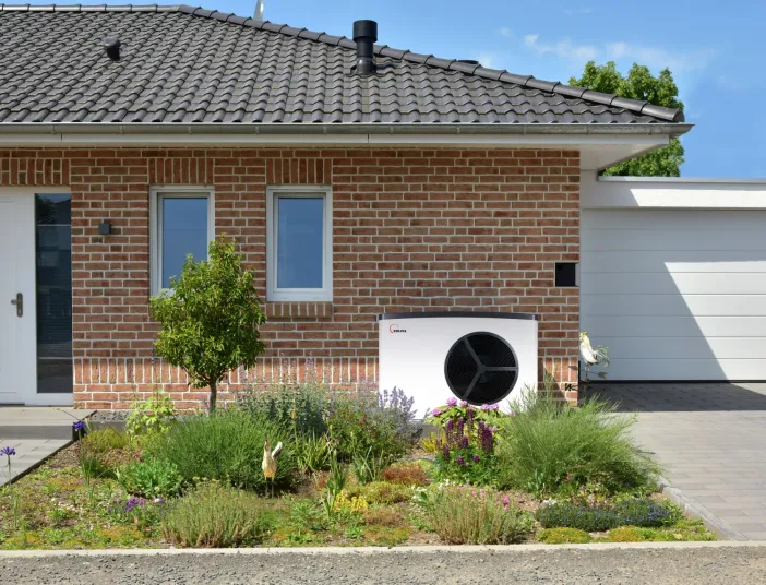 Wärmepumpe SolvisMia vor einem Einfamilienhaus aus Ziegeln mit Vorgarten.