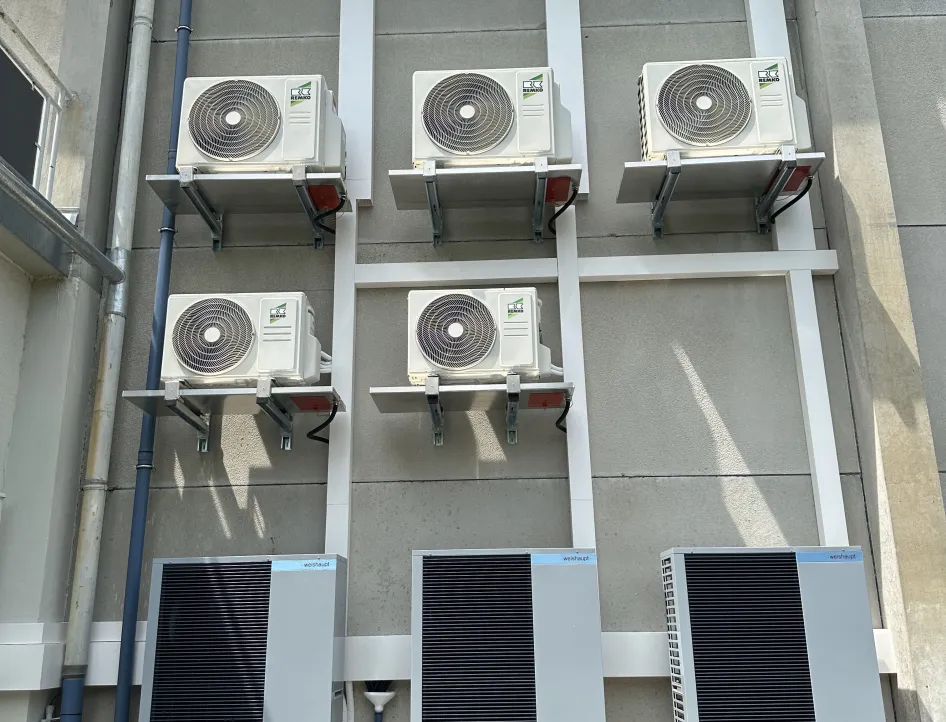 An der Fassade eines Gebäudes sind mehrere Klimageräte der Marke Remko in zwei Reihen übereinander montiert. Darunter befinden sich drei größere graue Wärmetauscher- oder Technikmodule, die ebenfalls an der Wand befestigt sind.